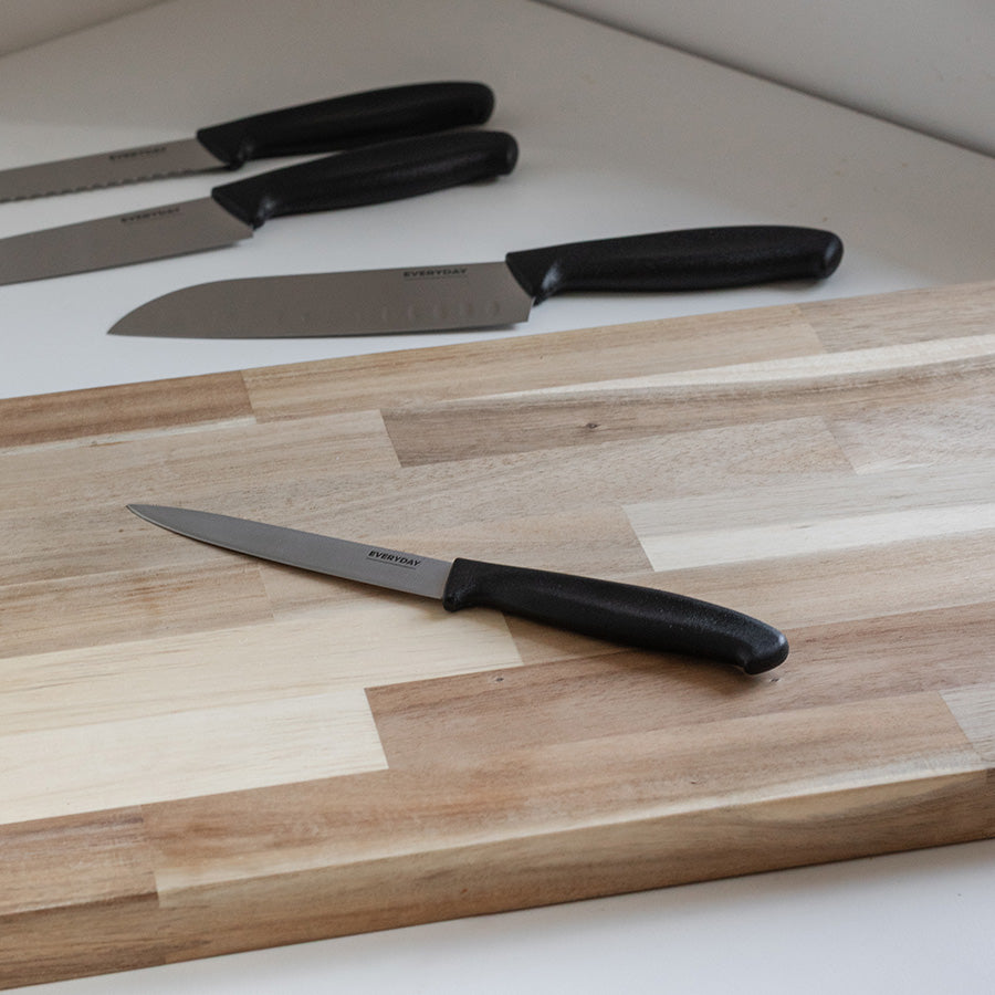 Everyday Cut universalkniv plassert på en skjærefjøl sammen med andre kniver, med fokus på det ergonomiske håndtaket.