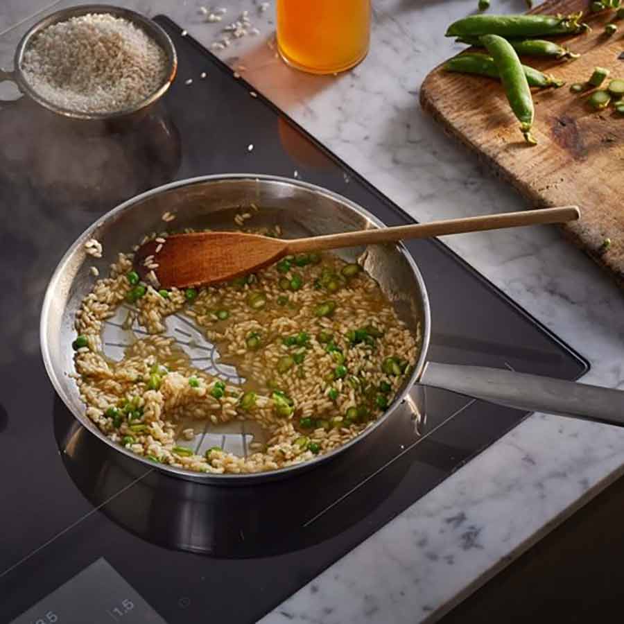 All Steel Pure stekepanne fra Fiskars Kjøkken med risotto som tilberedes, visende matlagingsprosess i en moderne kjøkkeninnredning.