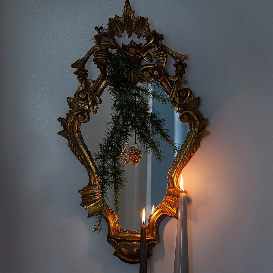 Julepynt hengt opp på en speilramme, med grønne elementer og stearinlys som skaper en koselig atmosfære.