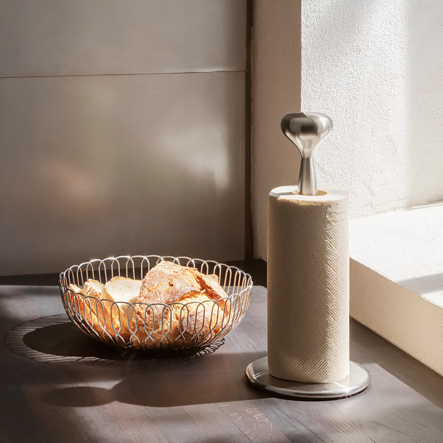 Brødkurv med nybakte rundstykker, plassert på et bord med en papirhåndkleholder i bakgrunnen, fra Georg Jensen.
