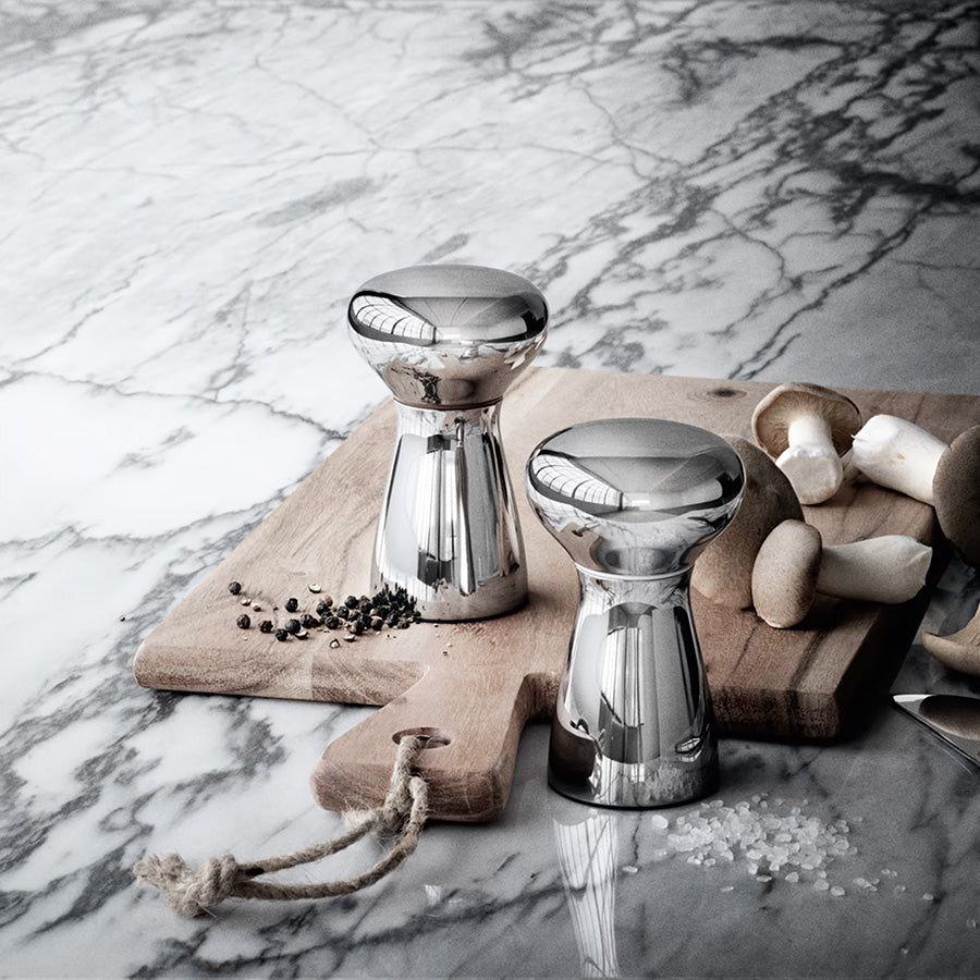 Salt- og pepperkvern i blankt rustfritt stål fra Georg Jensen, med ferske krydder og sopp på et trebrett.