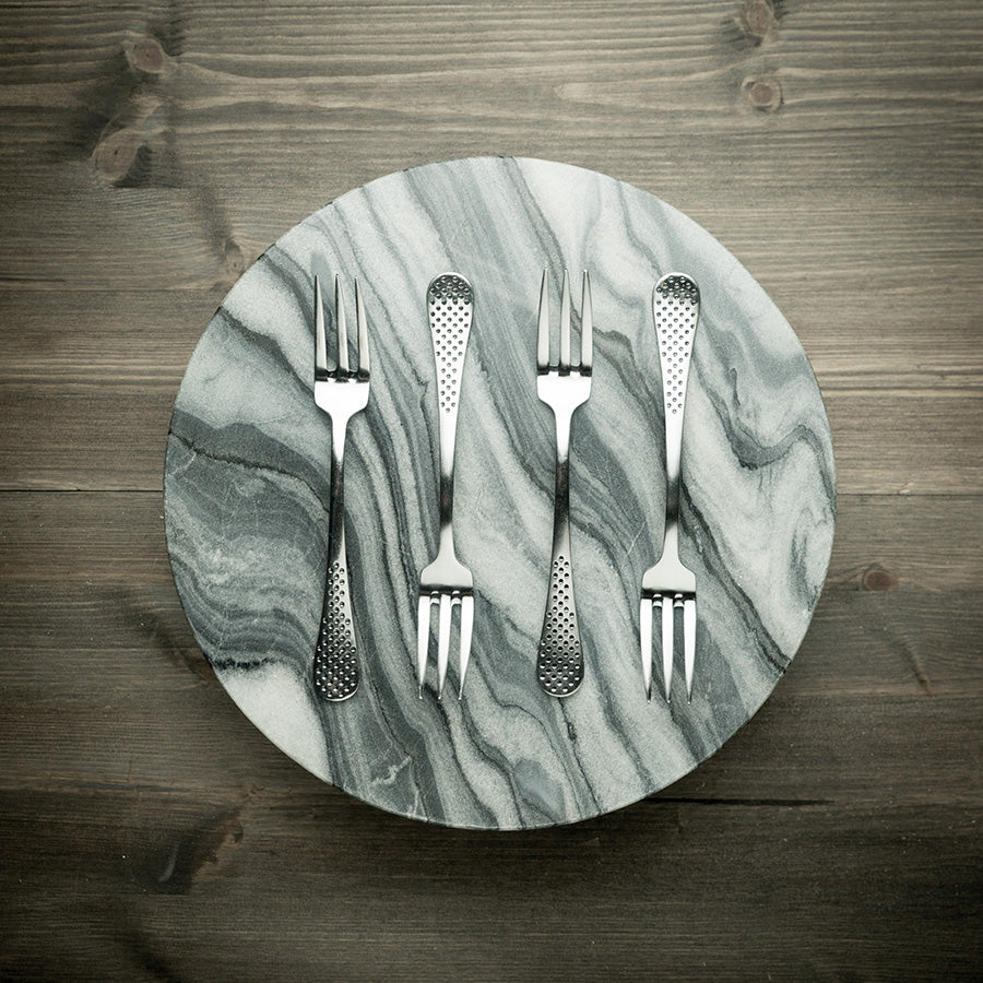 Fire stilige gafler plassert på en moderne marmorplate, fremhever det tidløse designet og kvaliteten til Globals gaffelsett, ideelle for enhver middag.