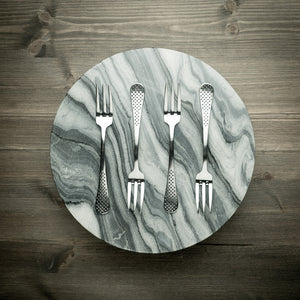 Fire stilige gafler plassert på en moderne marmorplate, fremhever det tidløse designet og kvaliteten til Globals gaffelsett, ideelle for enhver middag.