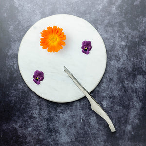Global pinsett med blomster og urter på en marmorplate, ideell for finpussing og detaljering av anretninger.