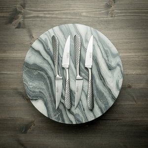 Fire stekekniver fra Global plassert på en marmorplate, fremhevende den elegante designen og skarpe eggen, perfekt for matentusiaster.