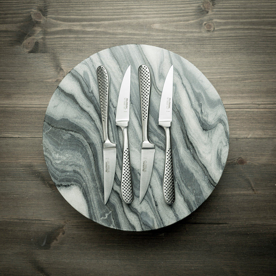 Fire stekekniver fra Global plassert på en marmorplate, fremhevende den elegante designen og skarpe eggen, perfekt for matentusiaster.