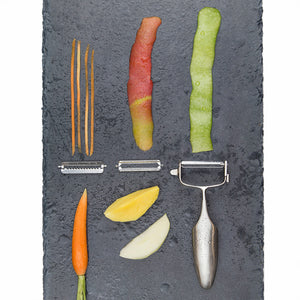 Various vegetable peelings and the Global Gs-94 skreller på en steinbordplate. Illustrerer bruken av skrelleren med ulike typer grønnsaker og frukt.