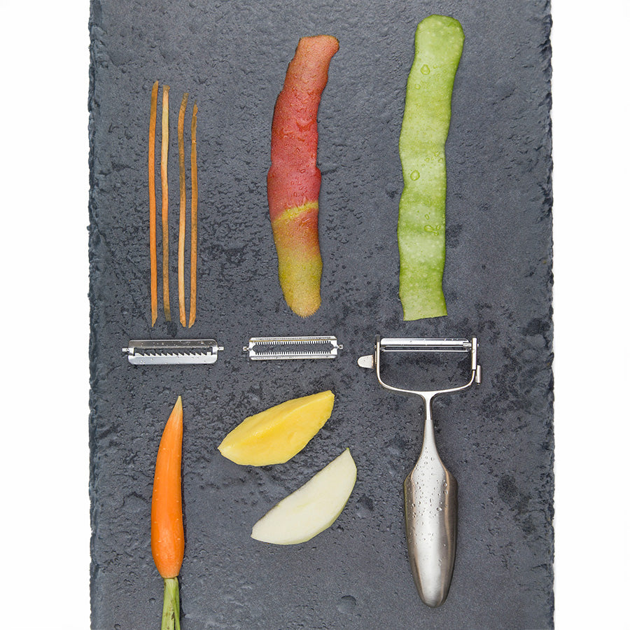 Various vegetable peelings and the Global Gs-94 skreller på en steinbordplate. Illustrerer bruken av skrelleren med ulike typer grønnsaker og frukt.
