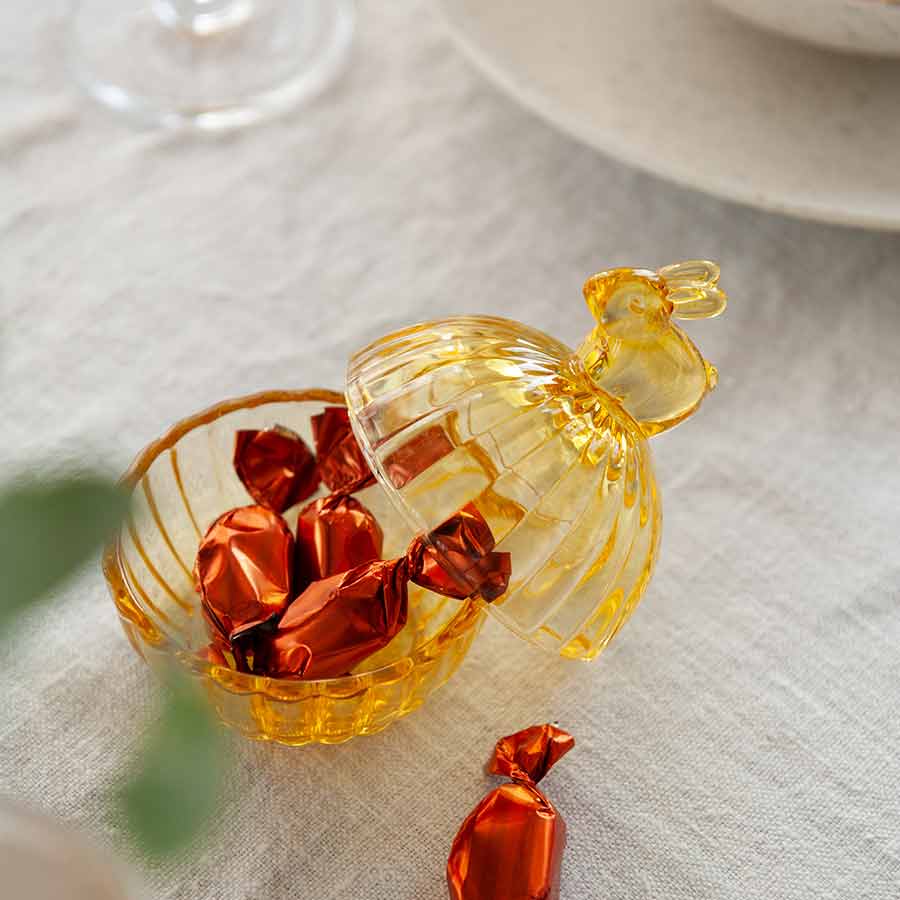 Hadeland Glassverk gul glasskål med lokk åpnet, fylt med glitrende innpakket godteri, perfekt for påskefeiring.