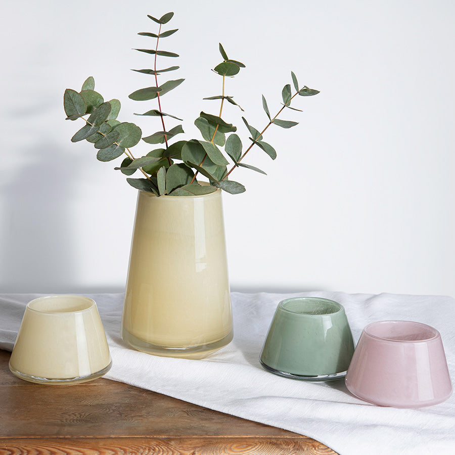 Stilfull Hadeland Glassverk Dugg vase i gul farge med eukalyptus, omkranset av fargekoordinert småvaser, på et lyst underlag.