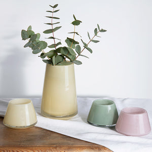 Stilfull Hadeland Glassverk Dugg vase i gul farge med eukalyptus, omkranset av fargekoordinert småvaser, på et lyst underlag.