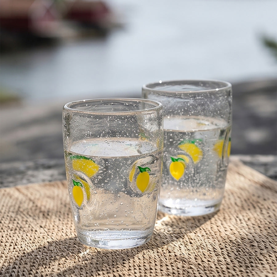 To Hadeland Glassverk drikkeglass med sitronmotiv fylt med bobler, ideelt for forfriskende drikker ved vannkanten.