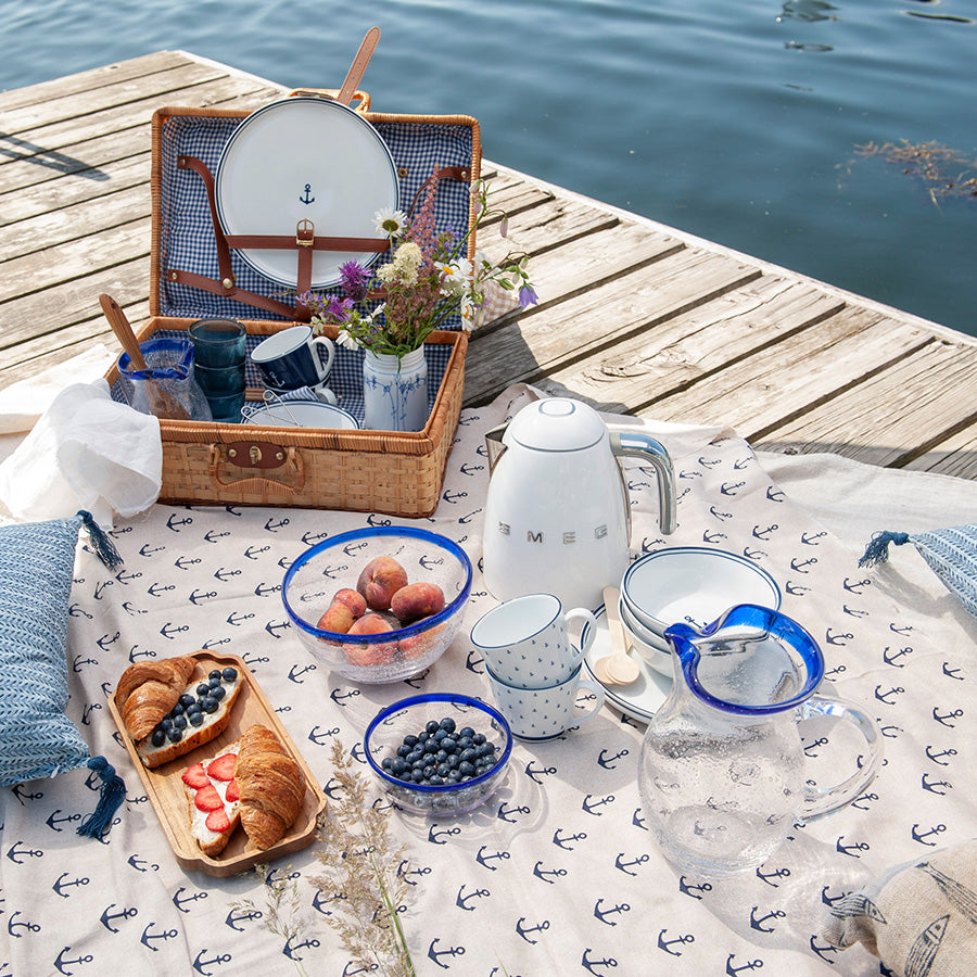 Hadeland Glassverk Skjærgård mugge på piknik med forskjellige retter, omringet av en vakker naturlig setting.