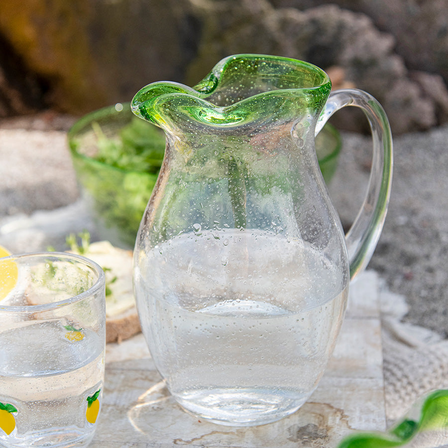 Sommereng mugge fra Hadeland Glassverk, fylt med klart vann, med en karakteristisk grønn kant som gir et friskt sommerpreg.