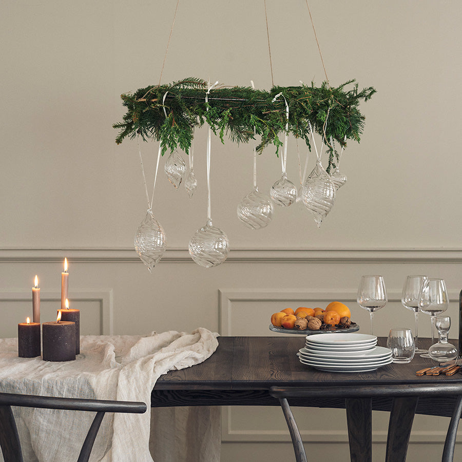 Klar glasskule med optikkmønster som julepynt i en dekorativ vintergrønn girlander over spisebordet