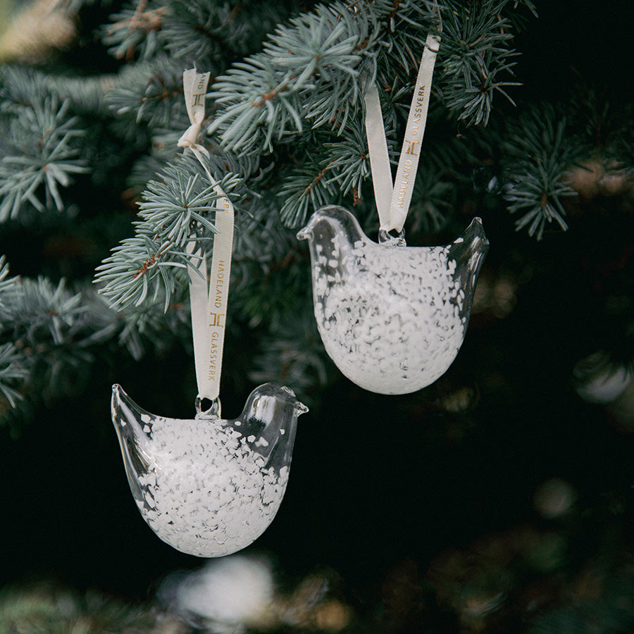 To hvite, spettet glassornamenter formet som turtelduer henger sammen på en grangren