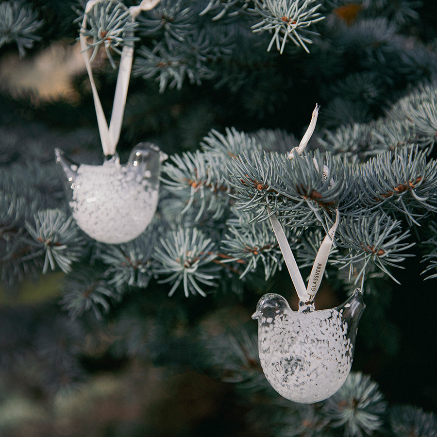 To hvite turtelduer i spettet glass henger som julepynt på et grantre