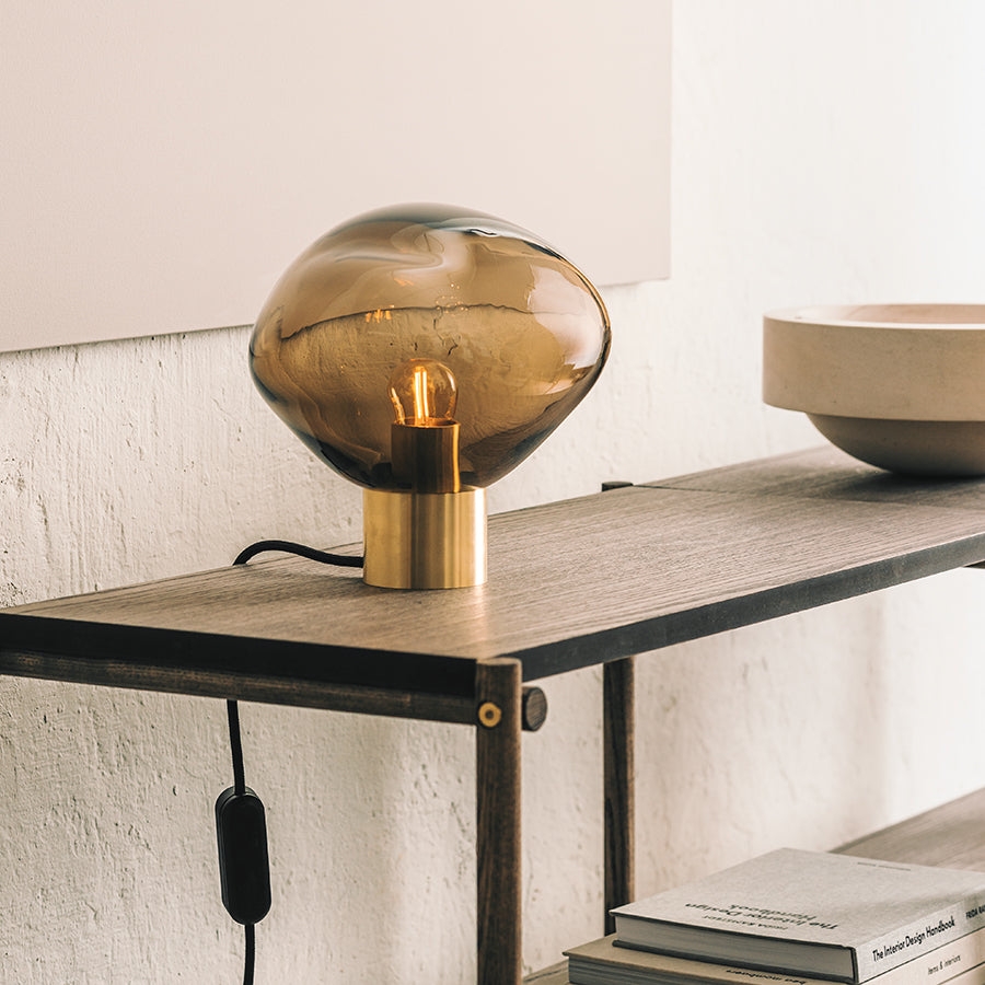Hadeland Glassverk Crystal Stone bordlampe Kakao plassert på en moderne hylle, gir varmt lys og stil til innredningen.