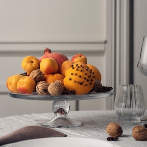 Klart kakefat på stett med frukt, nøtter og dekorativ appelsin