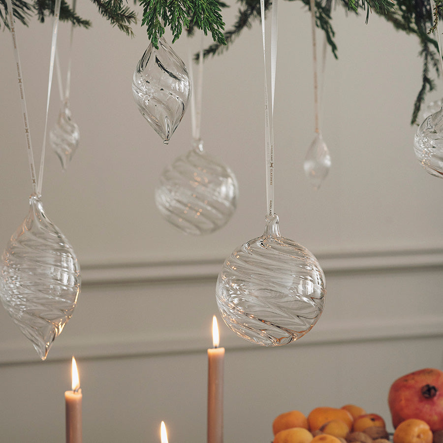 Klare julekuler i optikkglass henger på en julegren over tente lys
