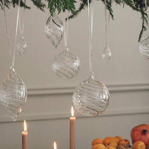 Klare julekuler i optikkglass henger på en julegren over tente lys