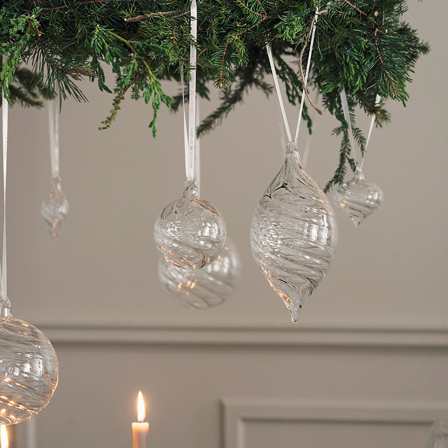 Elegante klare julekuler i optikkglass pyntet på en grønn julegren