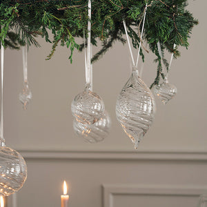 Elegante klare julekuler i optikkglass pyntet på en grønn julegren