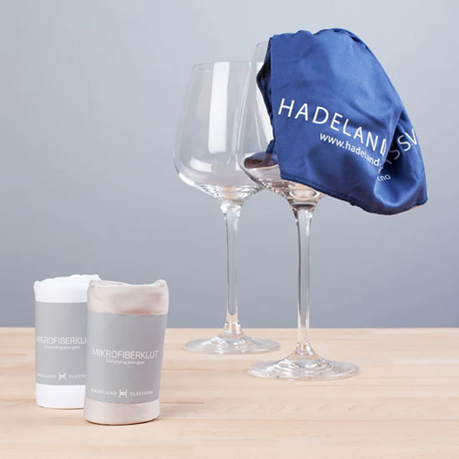 To Hadeland Glassverk glasskluter i blått og hvitt ved siden av elegante vinglass, ideelt for glasspleie.