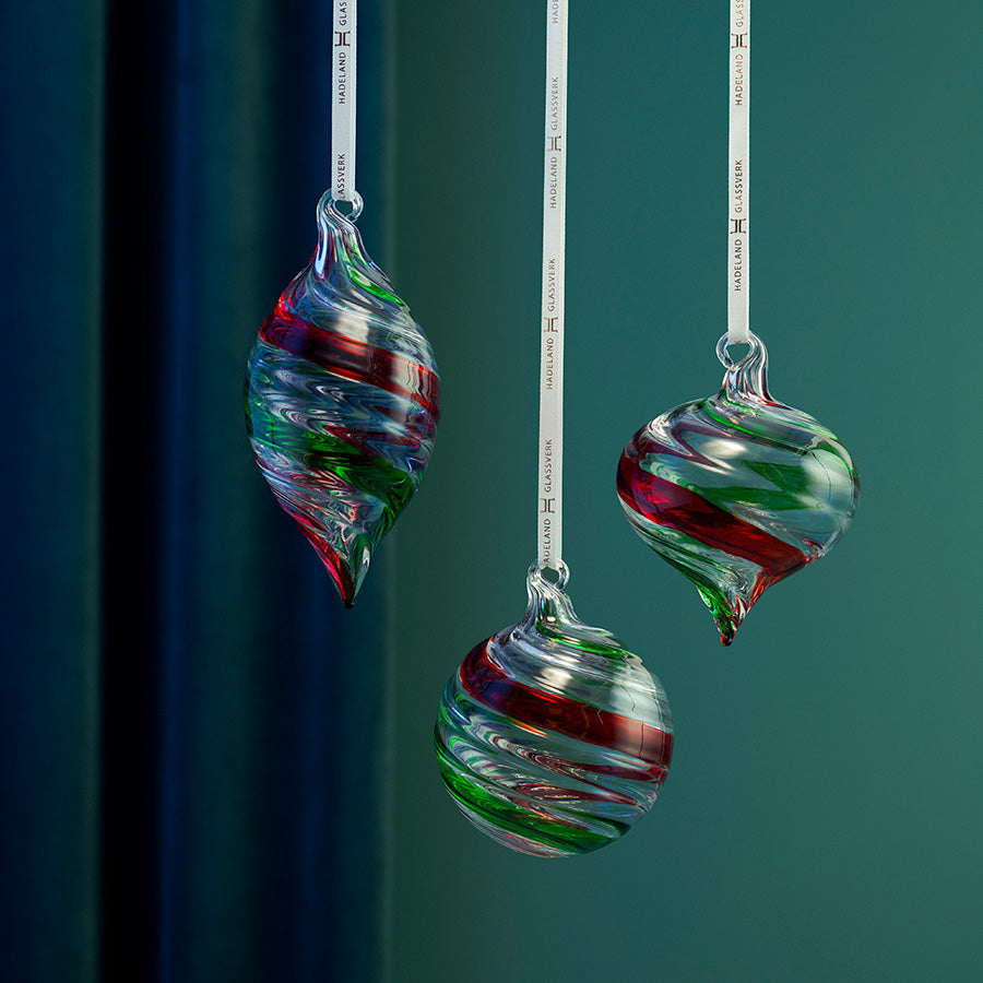 Tre dekorative glasskuler i rødt og grønt med spiraldesign, vist hengende mot grønn bakgrunn
