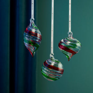 Tre dekorative glasskuler i rødt og grønt med spiraldesign, vist hengende mot grønn bakgrunn