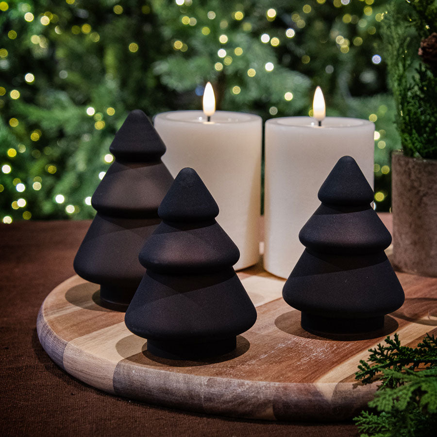 Flere små frostede glass juletre i kakao-farge fra Hadeland Glassverk, omgitt av stearinlys, skaper en koselig julestemning.