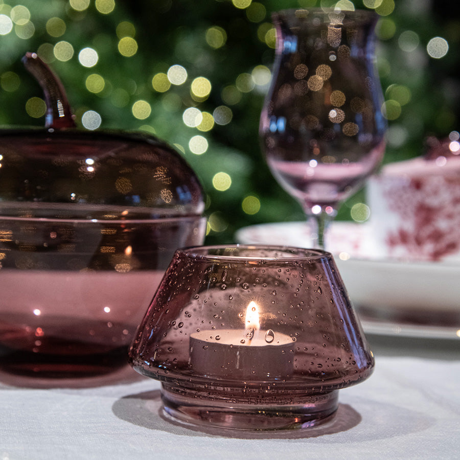 Hadeland Glassverk rosa lyslykt med tent telys, dekorert med julepynt og varm bakgrunnslyssetting.