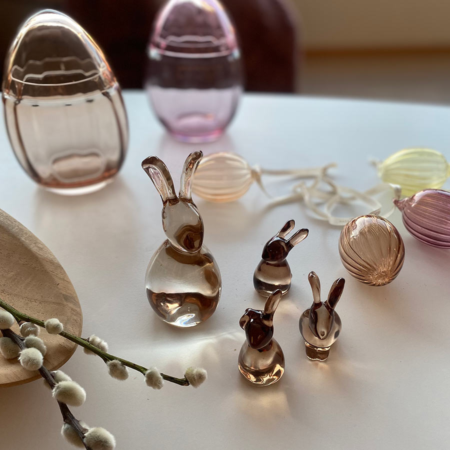 A creative collection featuring glass Hare figurines from Hadeland Glassverk, alongside colorful egg decorations on a table.