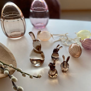 A creative collection featuring glass Hare figurines from Hadeland Glassverk, alongside colorful egg decorations on a table.