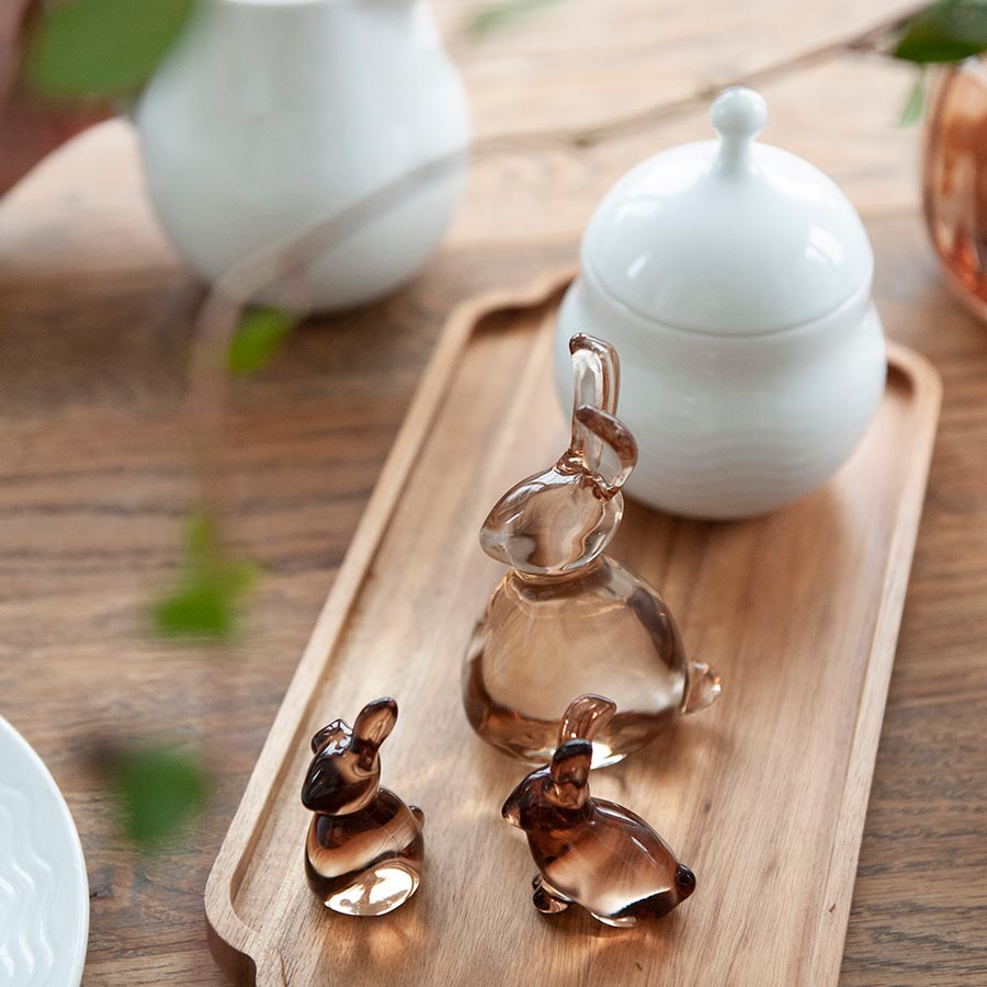 An inviting display of glass Hare figurines from Hadeland Glassverk, with a hand reaching for one on a wooden tray.