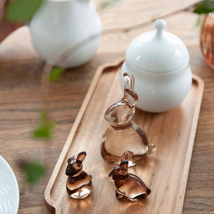 An inviting display of glass Hare figurines from Hadeland Glassverk, with a hand reaching for one on a wooden tray.