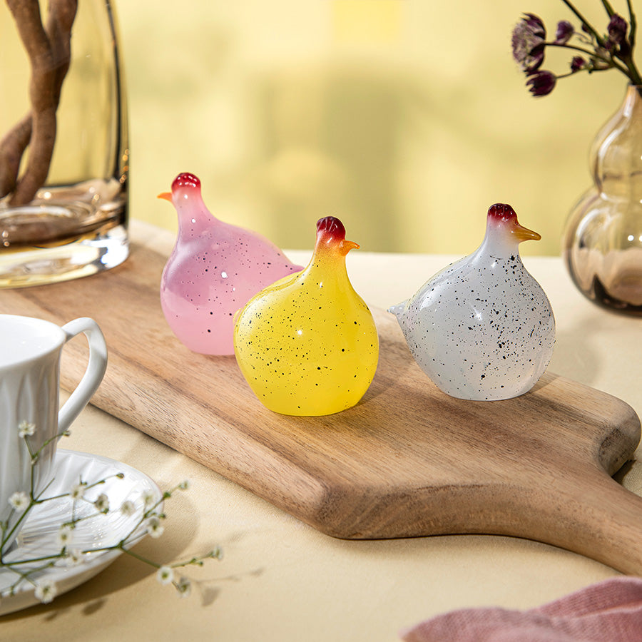 Tre ulike fargede glasshøner - gul, rosa og hvit - i et stilrent stilleben, designet av Hadeland Glassverk.