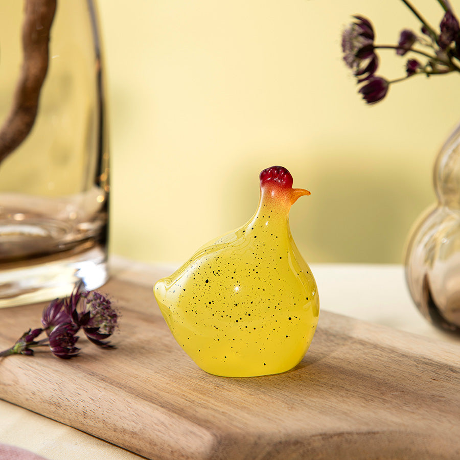 Gul glasshøne fra Hadeland Glassverk plassert på et bord, gir en lys og innbydende atmosfære.