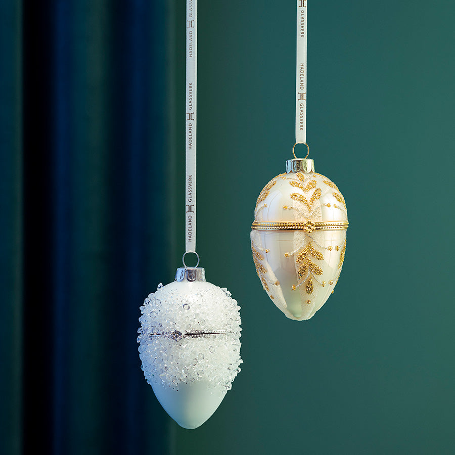 Gullfarget juleegg med lokk henger sammen med et hvitt juleornament