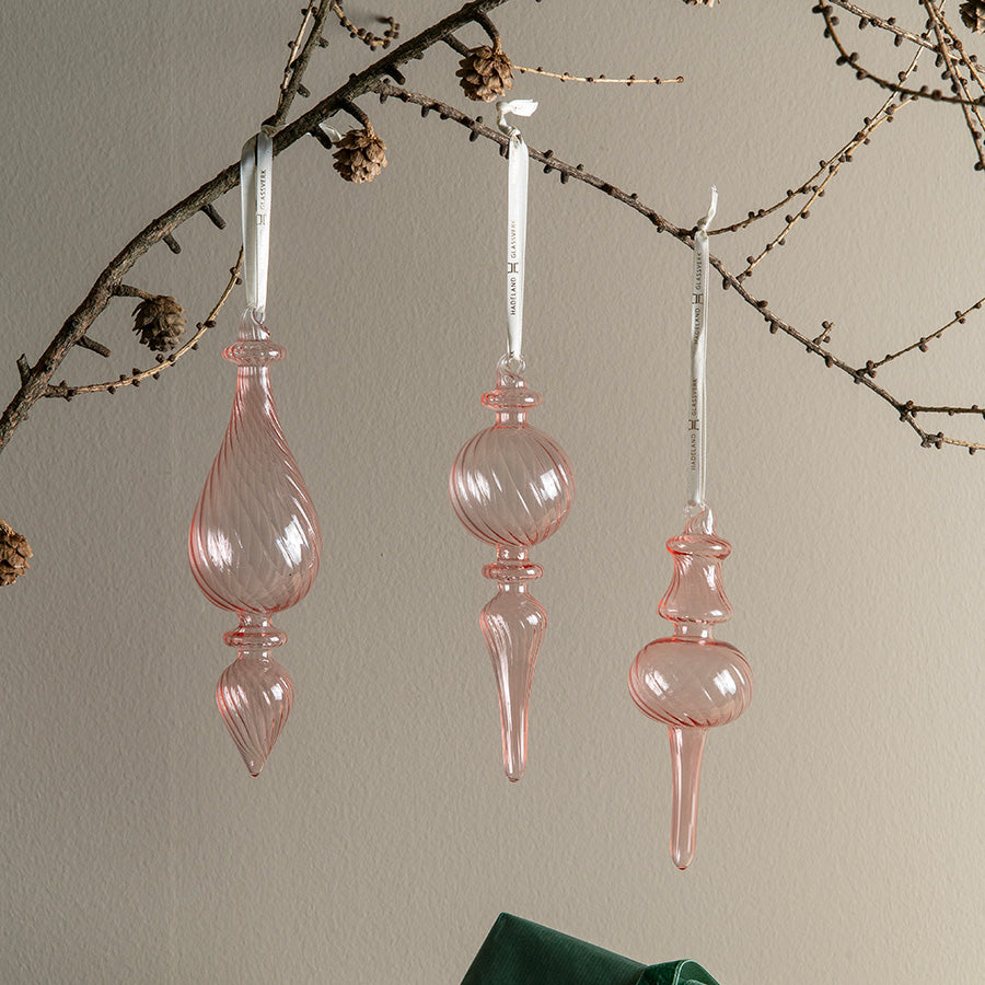 Tre rosa ornamenter fra Hadeland Glassverk Julefryd Optikk henger dekorativt på en gren