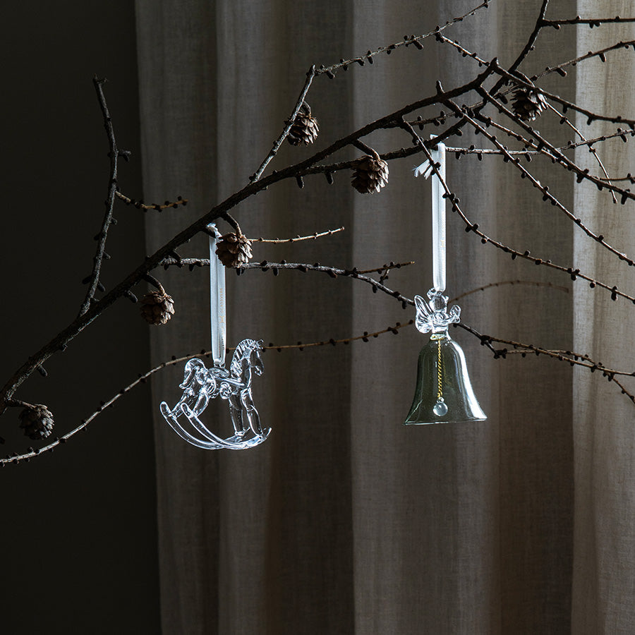 Dekorative glassheng med gyngehest og juleklokke på en gren i stemningsfull julebelysning