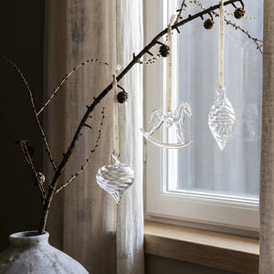 Klare glassheng fra Hadeland Glassverk dekorert på en gren foran et vindu med naturlig dagslys