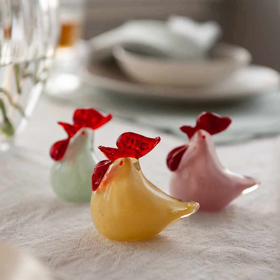 Nærbilde av tre Hadeland Glassverk glasshøner i ulike farger, med fokus på detaljer og borddekor.
