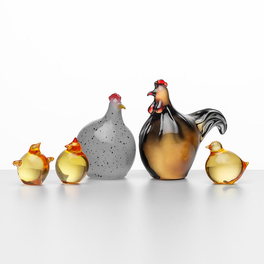 Elegant påskepynt fra Hadeland Glassverk, inkludert en hane, en høne og tre kyllinger i glass som reflekterer lys.