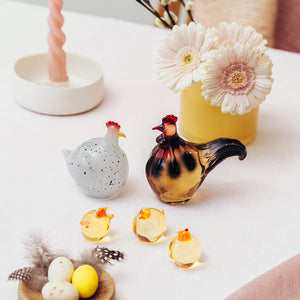 Vakkert arrangert påskepynt, med Hadeland Glassverk hane og høne sammen med glasskyllinger og en blomsterdekorasjon.