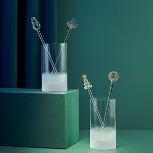 Dekorative rørepinner i glass med julefigurer og gulldetaljer i elegante drikkeglass