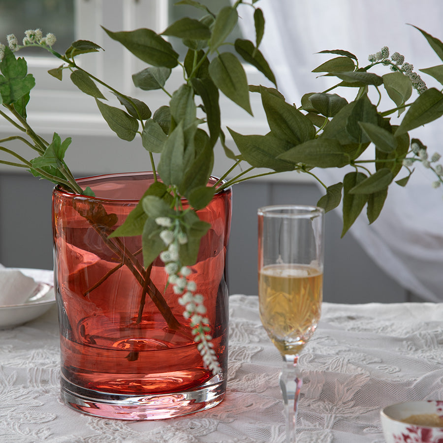 Hadeland Glassverk tulipanvase fylt med grønne grener, plassert på et dekket bord, og fremhever vaseformens elegante design.