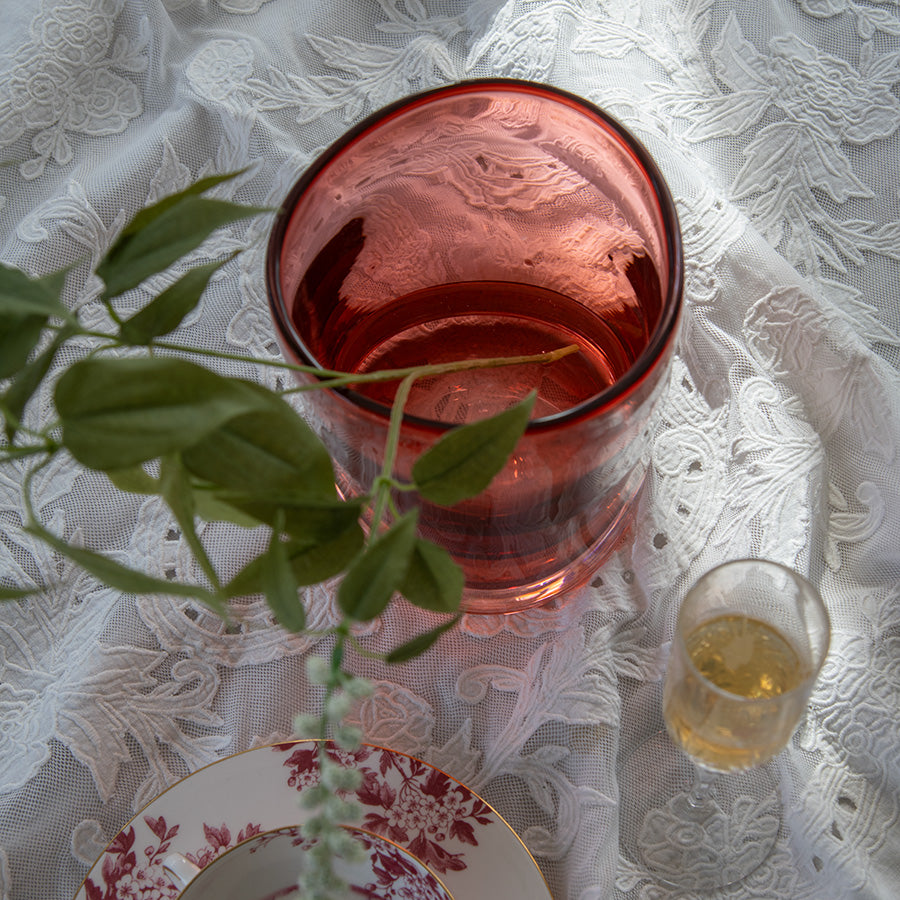 Overhodebilde av Hadeland Glassverk tulipanvase som viser den dype røde fargen, med grønne grener og dekorativt servise.