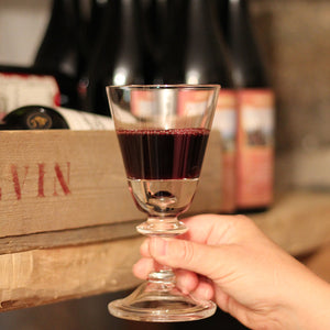 Tangen 25 cl glass fra Hadeland Glassverk fylt med rødvin, håndholdt foran vinkasser