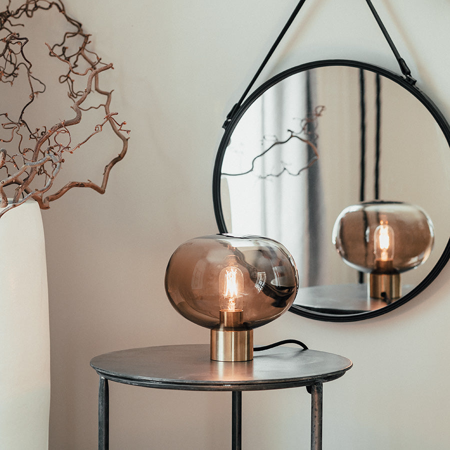 Bordlampe med munnblåst glasskuppel plassert på en bordoverflate, sammen med et speil. Den moderne designen kombinerer stil og funksjonalitet.